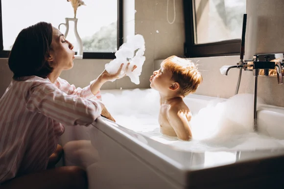 Person bläst Kind im Schaumbad Schaumbläschen entgegen